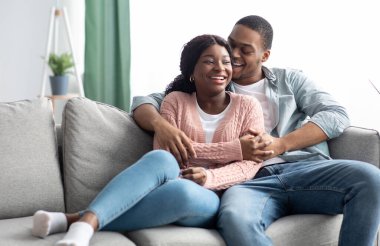 Neşeli siyah aile kanepede dinlenirken kucaklaşıp gülüyor.