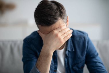 Evdeki kanepede oturan, başı ağrıyan bir adam.