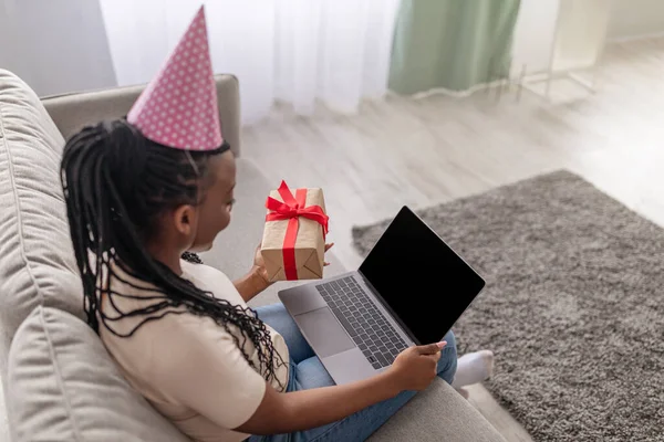 Young black woman with party hat and present using laptop