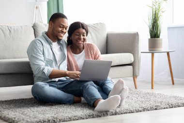 Yerde dizüstü bilgisayarla oturan mutlu siyahi aşıklar