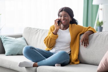 Güzel Afrikalı Amerikalı kadın koltukta oturuyor, telefonda konuşuyor.