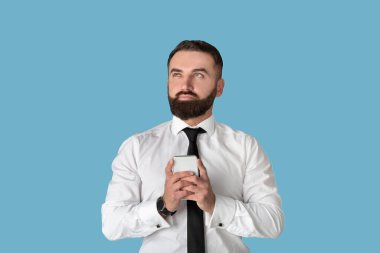 Çevrimiçi iş için akıllı telefon kullanan ya da mavi stüdyo geçmişine karşı iletişim kuran düşünceli bir ofis çalışanı.