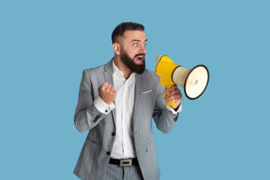Telaşlı genç iş adamı mavi stüdyo arka planında megafona bağırıyor.