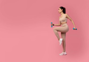 Pastel arka planda Dambıllarla Egzersiz Yapan Genç Kadın