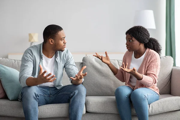 Evdeki kanepede oturan siyah kadın ve erkek kavga ediyor.