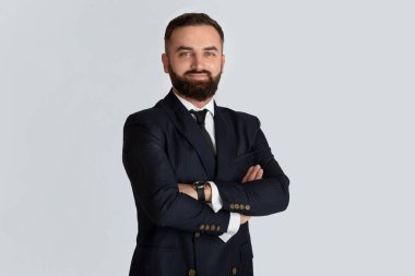 Formalite icabı sakallı yakışıklı CEO açık gri arka planda çapraz kollarla ayakta duruyor.