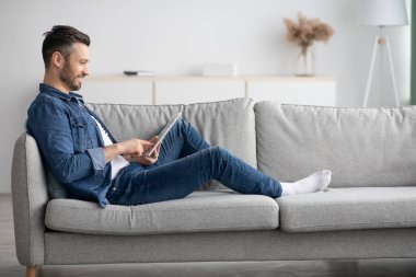 Dijital tablet kullanarak kanepeye yaslanan adamın yan görünümü