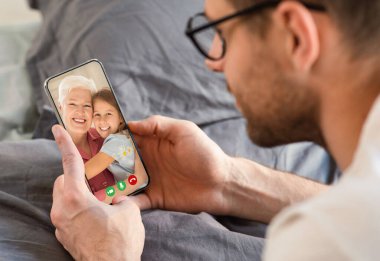 Ailesiyle iletişim kurmak için evde yatağında uzanan telefonu kullanan bir adam, hafta sonları online konferans.
