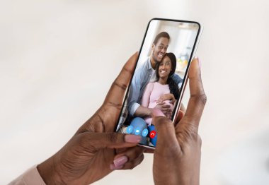 Tanımlanamayan Afrikalı Amerikalı kadın, arka planda genç bir çiftle görüntülü konuşma yapmak için akıllı telefon kullanıyor.