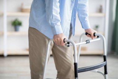 Evde çerçeveyle yürüyen yaşlı bir adamın görüntüsü, yakın plan. Profesyonel yardıma ihtiyacı olan engelli yaşlı kişi