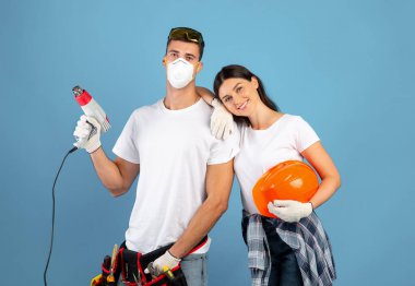 Genç çift tamir için hazır, mavi arka planda inşaat aletleriyle poz veriyorlar.