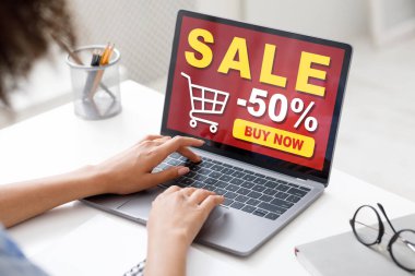 Siyahi kadın ofiste oturuyor, internetten alışveriş yapıyor, dizüstü bilgisayar kullanıyor.