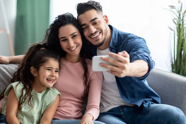 Arap adam, evde eşi ve kızıyla birlikte akıllı telefondan selfie çekiyor.