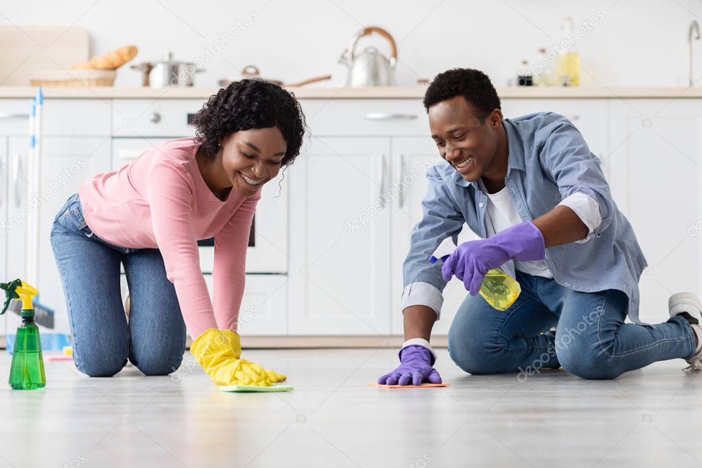 Cheerful african american couple cleaning floor together in kitchen