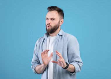 Mide bulandırıcı genç bir adam bir şeyi reddediyor, HAYIR işareti yapıyor ya da mavi stüdyonun arka planında duruyor.