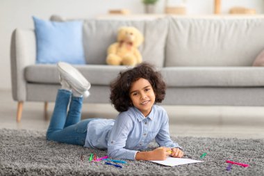 Renkli kalemlerle kağıda resim çizen Afrikalı Amerikalı bir kız.