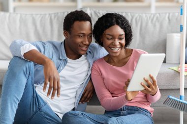 Oturma odasında dijital tabletle gülümseyen siyah aşıklar.