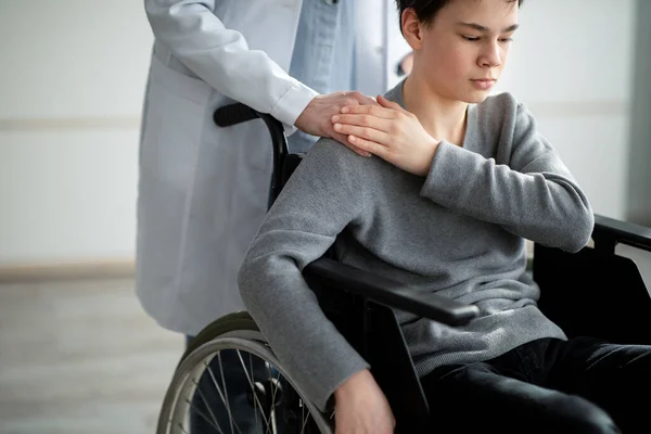 Handicapped teenage boy in wheelchair feeling depressed, nurse taking care of him at home, copy space