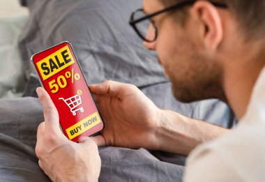 Cep telefonu kullanan adam evde uzanıyor, internetten satın alıyor.