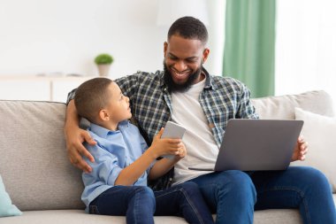 Afrika kökenli Amerikalı baba ve oğul akıllı telefon ve dizüstü bilgisayar kullanıyor.