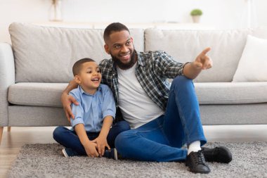 Afrikalı baba ve oğul evde yerde oturuyorlar.