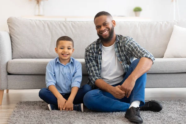 Black Father And Son Posing Sitting On Floor At Home