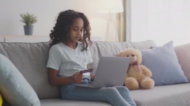 Erken dönem finansal okuryazarlık. Genç Afro-Amerikalı kız internetten bilgisayar ve kredi kartıyla alışveriş yapıyor.