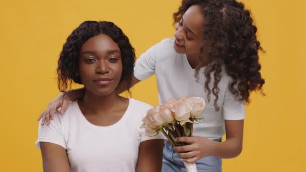 Jeune mère afro-américaine obtenant un bouquet de fleurs de sa fille mignonne, profitant de la surprise, fond orange — Video