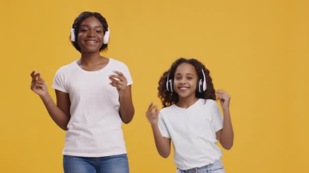 アフリカ系アメリカ人の母親と娘のワイヤレスヘッドフォンダンスと指を一緒にスナップ、オレンジの背景 — ストック動画
