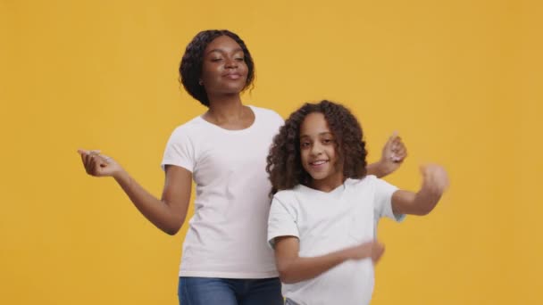Glad svart mamma och dotter dansar tillsammans, har roligt över orange bakgrund, slow motion — Stockvideo