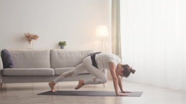 Aktif, esnek bir kadın evde yoga yapıyor, pilates yapıyor, bacağını kaldırıyor, yavaş çekim yapıyor.