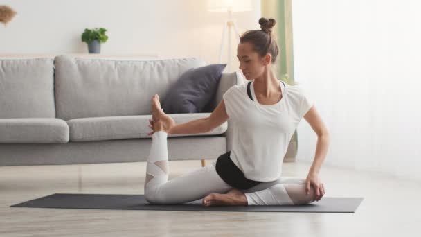 Pratique de yoga. Jeune femme flexible étirant sa jambe, faisant de l'exercice à l'intérieur de la maison, ralenti — Video