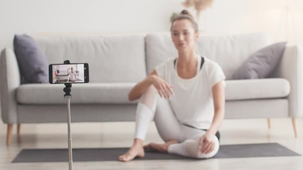 Fitness-Blog. Yoga-Trainer nimmt nützliches Video auf Smartphone auf, sitzt zu Hause auf dem Boden und spricht mit Kamera — Stockvideo