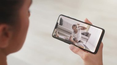 İnternetteki yoga pratiği. Genç bir kadının pilates dersleri izlerken ve akıllı telefondan esnerken yakın plan çekimleri.