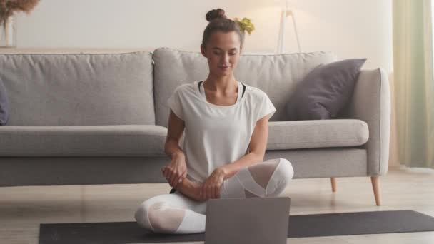 Online cvičení jógy. Mladá žena cvičí meditaci, video volá do skupin, mává rukou k notebooku a usmívá se — Stock video