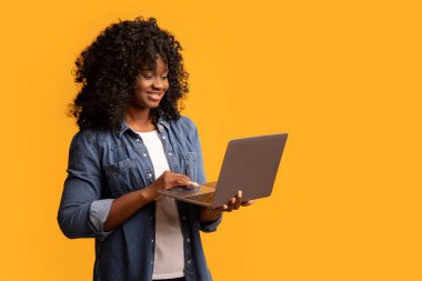 Sarı arka planda dizüstü bilgisayar kullanan güzel siyah bayan.