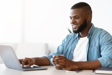 Bağımsız Kavram. Neşeli, siyah, serbest çalışan, kahve içen ve dizüstü bilgisayarda çalışan adam.