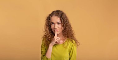 Sevimli kızıl saçlı kıvırcık kız parmaklarını dudaklarına bastırıyor ve sessiz şarkı söylüyor.