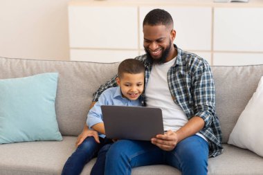 Afrikalı baba ve oğul dizüstü bilgisayarda çizgi film izliyorlar.