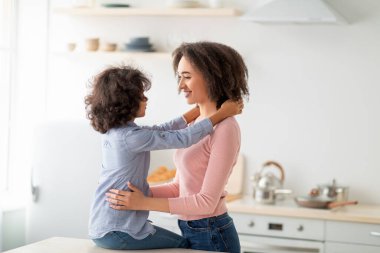 Afrikalı Amerikalı kız, gülümseyen annesine sarılıyor.