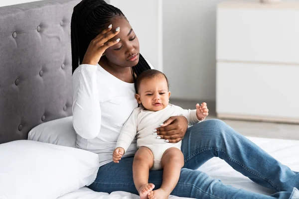 Tired African American mom sitting with kid on bed — Stock Photo, Image
