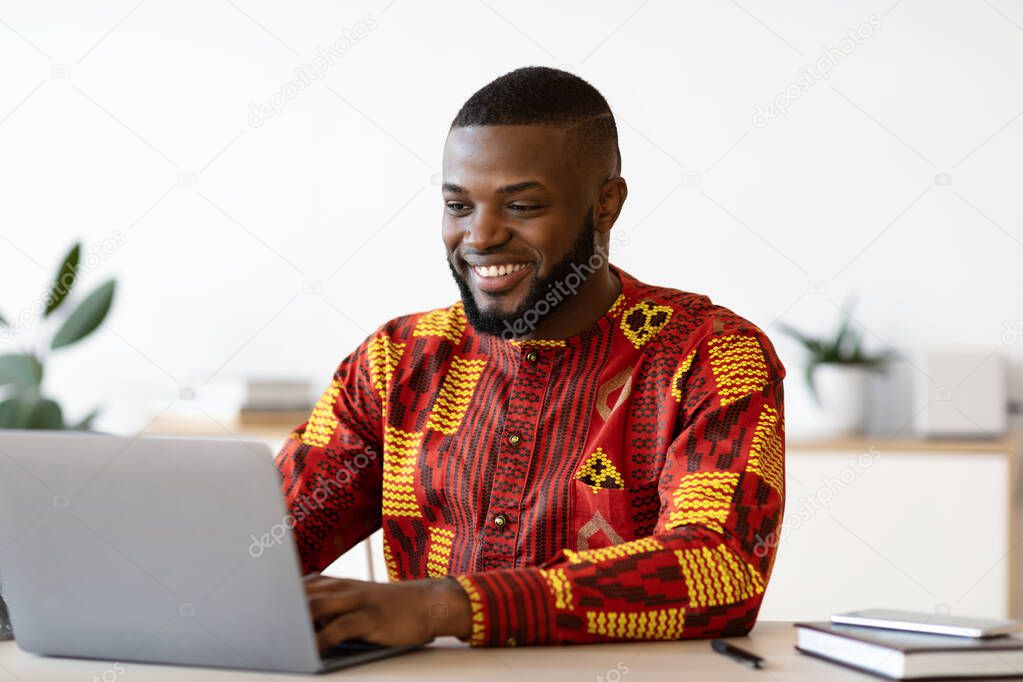 Successful Black Businessman In African Traditional Clothes Sitting At Workplace In Office