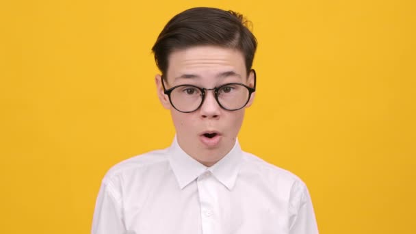 Geschokt tiener jongen kijken naar camera aanraken gezicht, gele achtergrond — Stockvideo