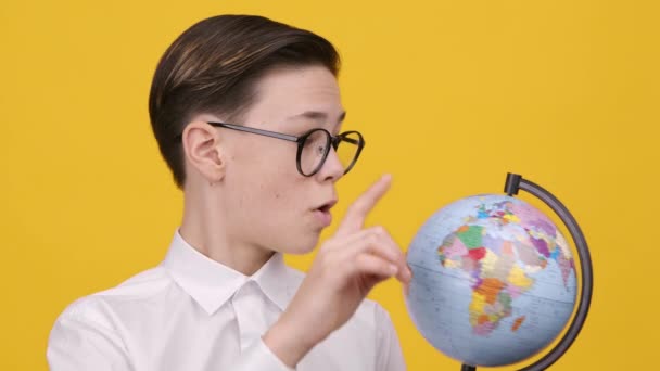 Школярка тримає Землю глобус вказуючи пальцем Вибираючи напрямок, жовтий фон — стокове відео