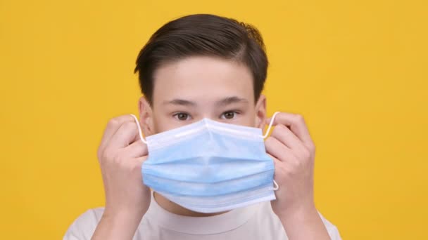 Adolescente niño usando máscara protectora de la cara de pie sobre fondo amarillo — Vídeos de Stock