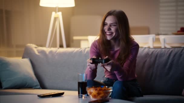 Νεαρή συναισθηματική κυρία παίζει βιντεοπαιχνίδια στο gamepad στο σπίτι, απολαμβάνοντας το βράδυ της Παρασκευής με σνακ, αργή κίνηση — Αρχείο Βίντεο