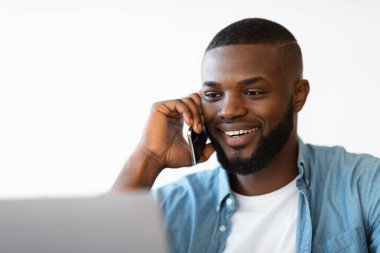 Neşeli Afrikalı Amerikalı Cep telefonuyla konuşan ve dizüstü bilgisayarla çalışan