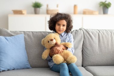 Gülümseyen siyah çocuk oyuncak ayıyı kucaklıyor.