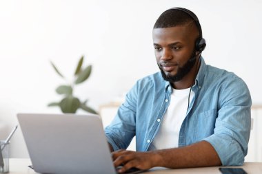 Ofiste dizüstü bilgisayarla çalışan kulaklıklı Afro-Amerikan bir adamın portresi.
