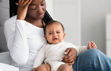 Stresli Afrikalı Amerikalı anne, çocuğuyla yatakta oturuyor.